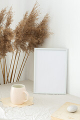 Home decor mock-up, blank picture frame near white painted concrete wall , dry Cane Reeds and old books