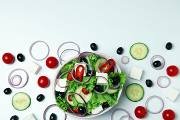 Bowl of greek salad and ingredients on white background, top view