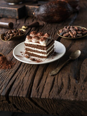 Slice of chocolate cake with tiramisu cream and cocoa powder on wooden table.