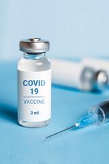 Coronavirus vaccine. Ampoules with coronavirus vaccine and a syringe on blue background. Covid-19 treatment. Vertical format