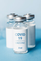 Coronavirus vaccine. Ampoules with coronavirus vaccine and a syringe on blue background. Covid-19 treatment. Vertical format