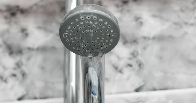 Tap water dripping out of used shower head in the bathtub close up shot traces of limescale deposits