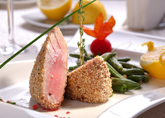 Tuna steak roasted with sesame and sided with cooked green beans on white plate, close-up.