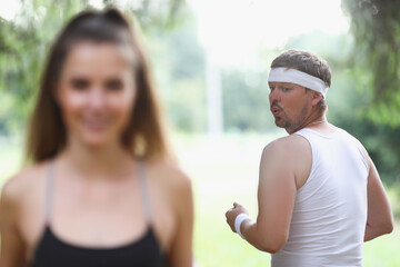 Fat man in sportswear looking at young girl jogging in park