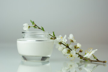 Fototapeta na wymiar Closeup of a jar of moisturizer and blooming flowers. Concept of spring skincare.