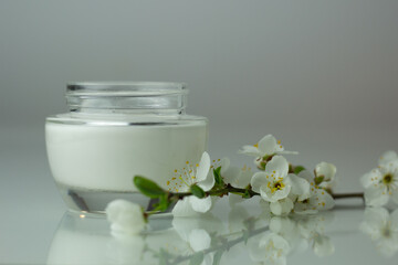 Fototapeta na wymiar Closeup of a jar of moisturizer and blooming flowers. Concept of spring skincare.