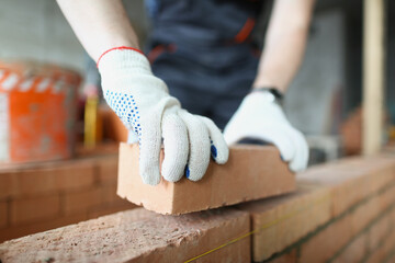 Man builder in protective gloves is building wall of bricks closeup