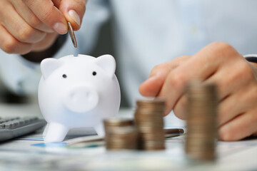 Man hand putting coin into white piggy bank closeup