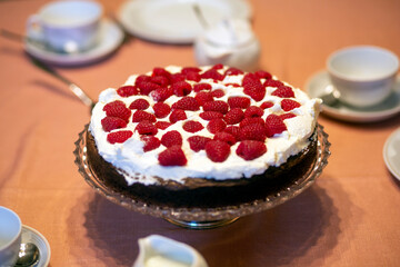 A birthday cake of chocolate, raspberries and cream on a table.