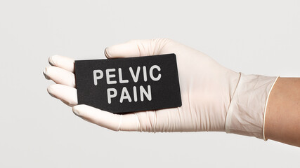 Closeup of the hand in a white sterile glove holding a card with text - Pelvic Pain