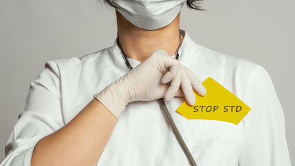 Cropped view of doctor in a white coat and sterile gloves holding a note with text - STOP STD