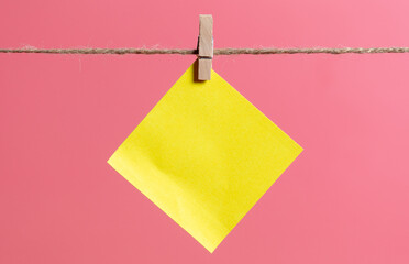 A yellow piece of paper hanging on a rope on a pink
