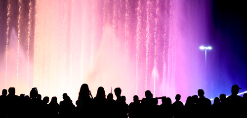 Silhouettes of people at a colored fountain at night.