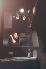 Young woman brushing hair in front of a bathroom mirror.