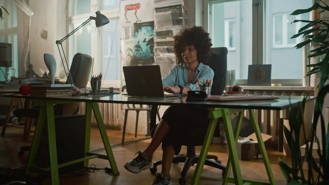 Young Female Specialist Sitting at Her Desk Works on Computer in Creative Office. Charmingly Authentic Professional works on Software Development, Game App Design, Social Media Marketing Project

