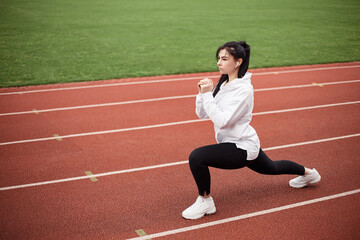 Girl stretches, prepares her body and muscles for a productive fitness workout. Flexible female dressed sports suit sporty model on the city stadium. Image with copy space. Single leg squats
