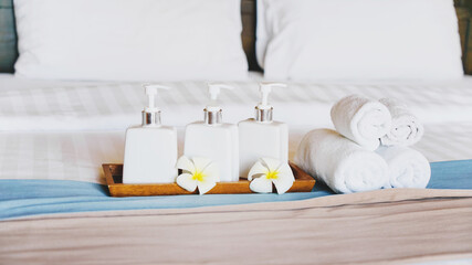 Fototapeta na wymiar bath accessories in white ceramic bottles ,blurred rolled towels and white blossom plumeria flower on hygiene comfortable bed in bedroom for spa ,recreation , hotel ,resort ,welcome guest concept