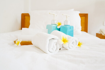 rolled white towels ,blurred bath accessories in blue ceramic bottles  and blossom plumeria flower  on hygiene comfortable bed in bedroom for spa ,recreation , hotel ,resort  ,welcome guest concept