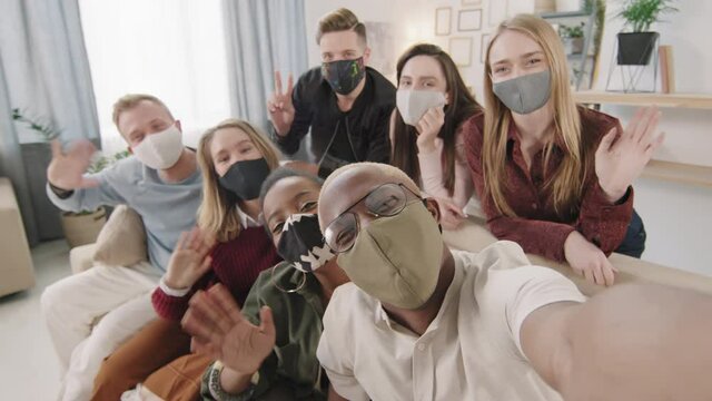 POV shot of group of young men and women in face masks taking selfie at get-together in apartment during pandemic