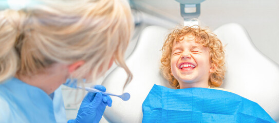 Pretty little boy in dental office, having his teeth checked by female dentist . - obrazy, fototapety, plakaty