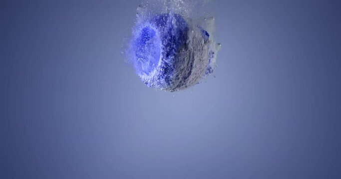 Colorful bath bomb falling down into clean water against blue background. Filmed in slow motion with RED camera
