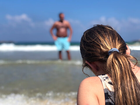 Girl sitting on the beach of Tel Aviv, Israel. Over the shoulder of a young lady sitting on the shore with a scary dark Man in the background. Blue sky and turquoise water in the beautiful summertime 
