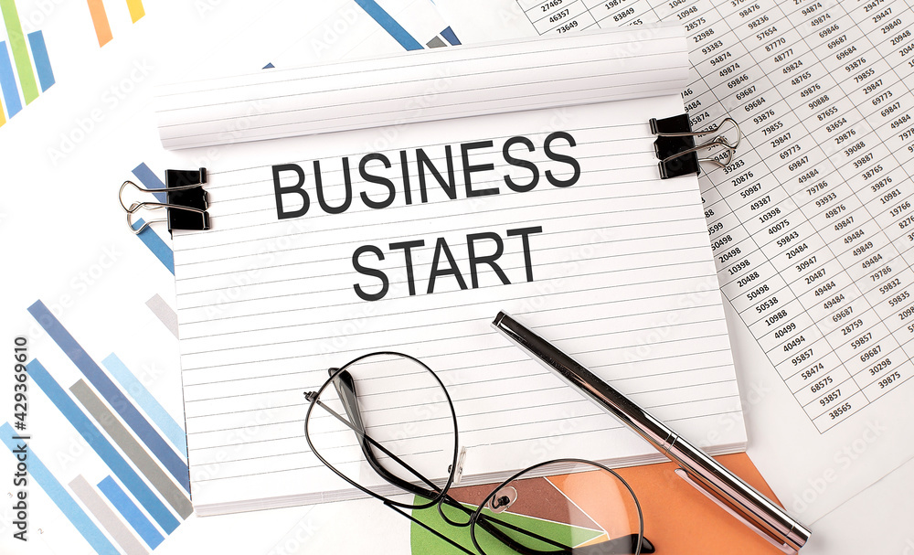 Poster notebook with text business start on table with charts,pen and glasses.
