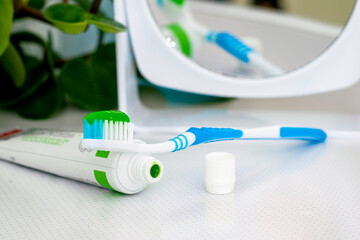 an open tube of toothpaste a toothbrush with applied toothpaste and a mirror on the dressing table