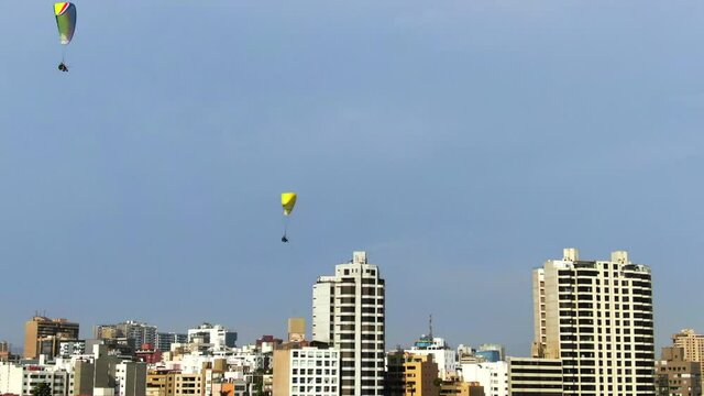 4k aerial daytime video of 2 paragliders flying over the coastal side of Lima in Miraflores, Peru. Coastline, skyscrapers and sports on a sunny summer day in the peruvian capital. Dolly out, 30fps