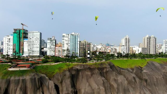 4k aerial video of 3 paragliders flying over the coastline of the pacific ocean in the green area of Miraflores, Lima, Peru. Recreational sports in a sunny summer day. Truck left to right, 30 fps