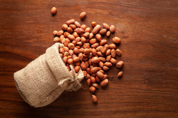 Close-up of organic red-brown peanuts (Arachis hypogaea)  spilled out from a laying jute bag over wooden brown background