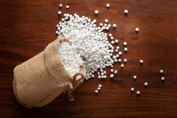 Close-up of organic white sago or sabudana big size spilled out from a laying jute bag over a wooden brown background. - obrazy, fototapety, plakaty