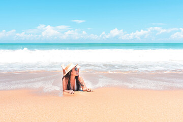 Fototapeta na wymiar Asian traveler woman wearing swimsuit, sunglasses and straw hat to lying on the beach in blue water