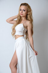Polish model posing with white top, long white dress with cut, showing her legs.
