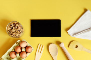 Flat lay with tablet with black mockup and place for text on yellow background. Food blogger's workplace. Culinary blog, recipe template, online cooking courses. Healthy food concept. Copy space.