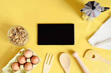 Flat lay with tablet with black mockup and place for text on yellow background. Food blogger's workplace. Culinary blog, recipe template, online cooking courses. Healthy food concept. Copy space.