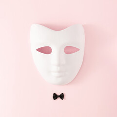 White costume ball face mask with black bow tie on bright pink background. Minimal abstract concept. Flat lay.
