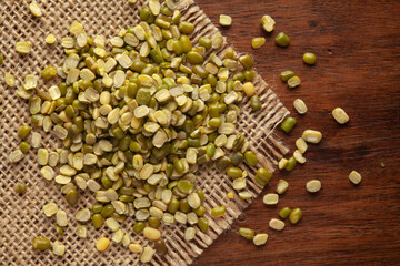 Macro Close-up of Organic split and unpolished Green Moong Dal (Vigna radiata) on Jute mat and wooden top.