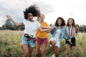 Four happy women hold hands and running on a field. Female friends having good times outdoors.