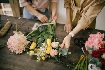 Two young women florist working in flower studio, making beautiful bouquet using fresh plants and flowers. - obrazy, fototapety, plakaty