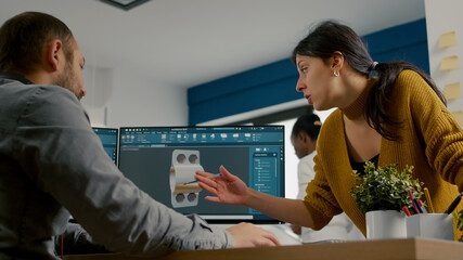 Industrial designer discussing with colleague while working in CAD program, designing 3D prototype of components. Woman engineer using pc with two monitors sharing ideas for construction mechanism