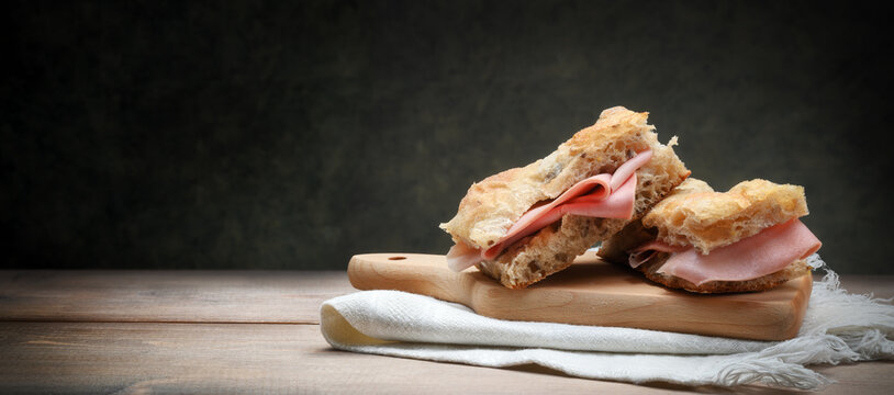 Focaccia with mortadella on old wooden table with cutting board and napkin, space for text.
