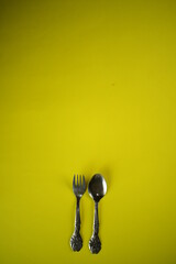 silver wares spoon and fork on bright yellow background