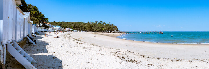 Panorama sur une plage de sable fin avec des cabanons et un ponton