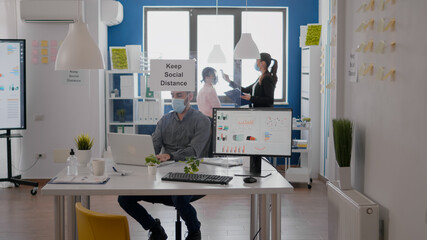 Freelancer wearing protective face mask checking team temperature using medical thermometer. Coworkers respecting social distance in new normal company office to avoid infection with virus disease