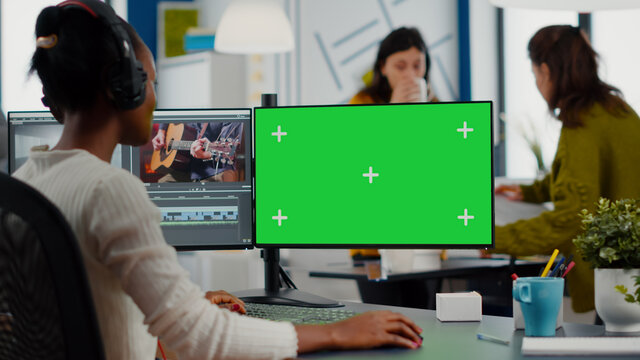 Black videographer using computer with chroma key, mock up isolated display editing video and audio footage. Woman editor processing film montage on green screen working in digital multimedia company