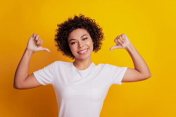 Portrait of young woman pointing finger herself on yellow background