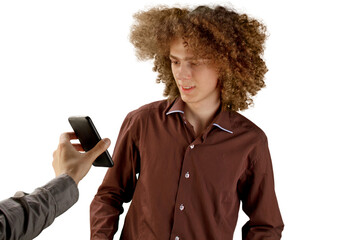 A long-haired curly-haired guy in a brown shirt on a white background uses a metal round comb. Emotions before a haircut in a hairdresser