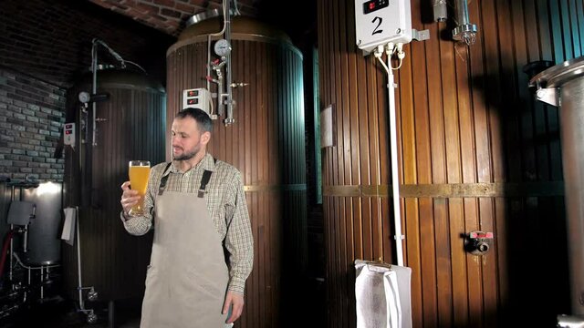 A specialist brewer stands and checks the quality of freshly squeezed beer from new-generation wooden barrels. A modern beer factory. Large wooden storage tanks. Brewery concept