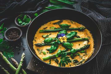 Omelette with green asparagus, basil and herbs on black background